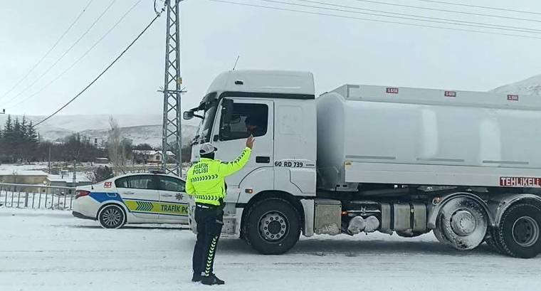 Karla kaplı yolda bir trafik polisi, büyük bir araca dur işareti yapıyor.