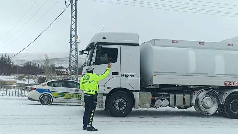 Karla kaplı yolda bir trafik polisi, büyük bir araca dur işareti yapıyor.