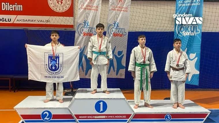 Dört çocuk sporcu madalyalarıyla podyumda duruyor; soldaki çocuk üzerinde kulüp arması bulunan bayrak tutuyor.