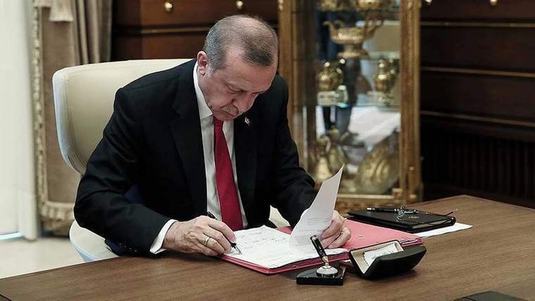 Bir masa etrafında oturan bir kişi, belgeleri inceliyor ve yazıyor.