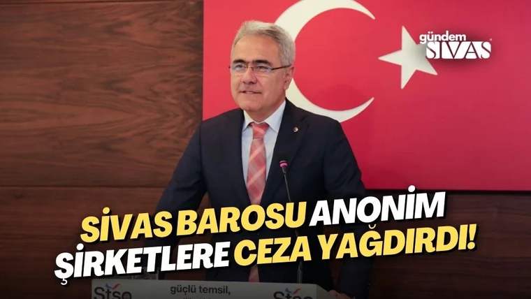 Kürsüde konuşan gözlüklü bir erkek, Türk bayrağı motifli kırmızı pano önünde duruyor.