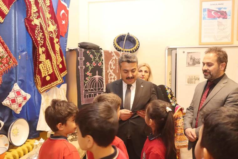 Bir grup çocuk, geleneksel kıyafetler ve el sanatları sergileyen bir stant önünde duruyor.