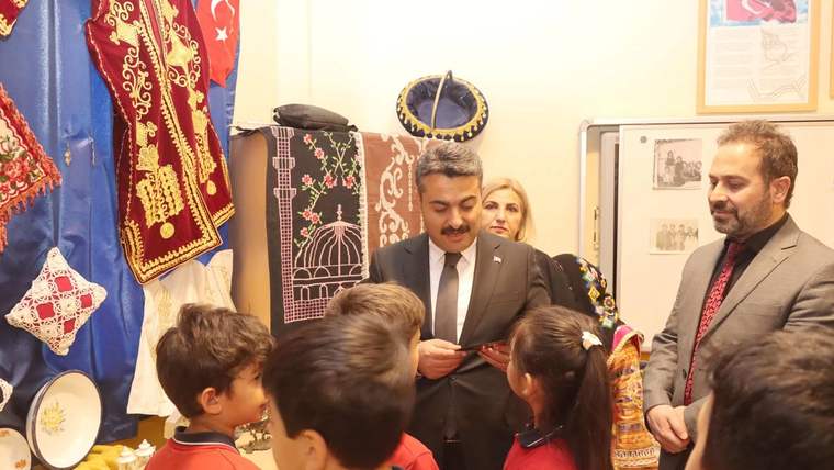 Bir grup çocuk, geleneksel kıyafetler ve el sanatları sergileyen bir stant önünde duruyor.