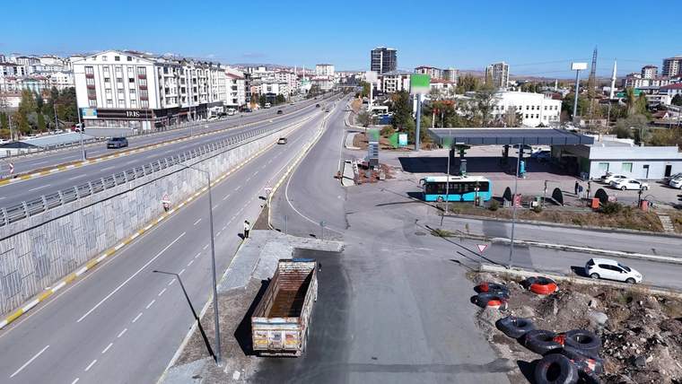 Boş bir yol, yan tarafında bir otobüs durağı ve bir benzin istasyonu görünmekte.