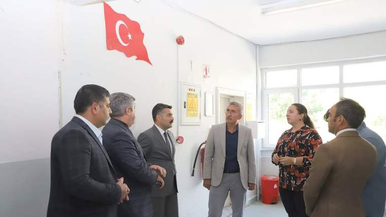 Okul koridorunda Türk bayrağının altında duran altı kişi, bir adamı dinlerken görülüyor.