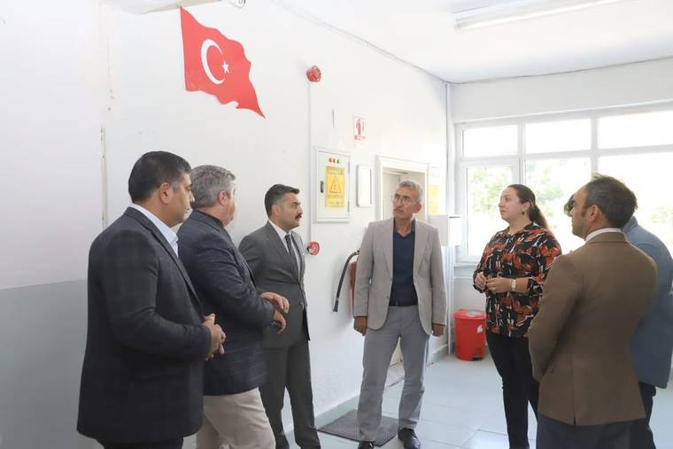 Okul koridorunda Türk bayrağının altında duran altı kişi, bir adamı dinlerken görülüyor.