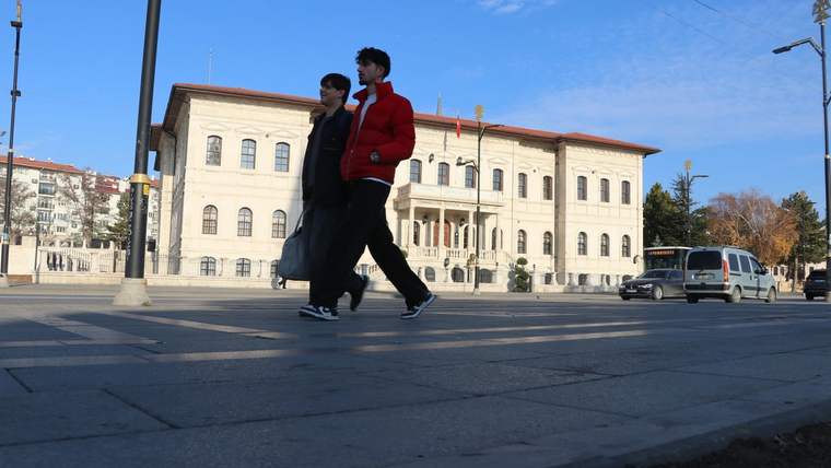 İki kişi, bir bina önünde yürüyerek geçiyor. Bina, klasik mimari tarzda inşa edilmiş.