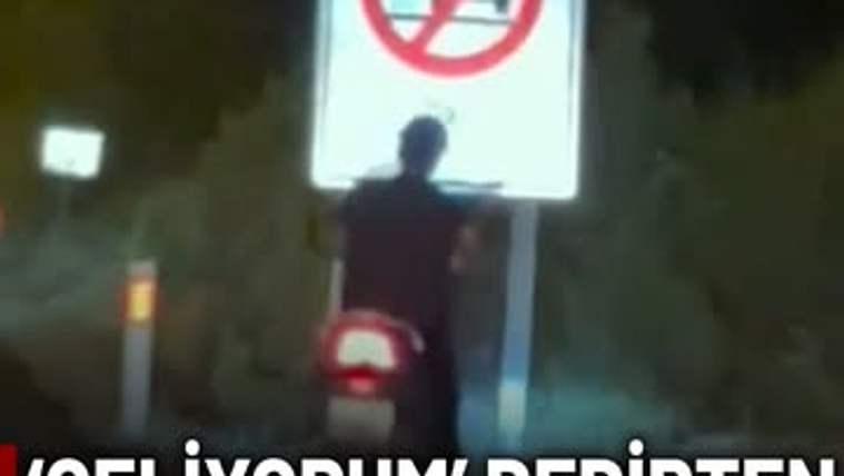 Motosiklet sürücüsü, yasak levhasına yaslanmış bir şekilde duruyor.
