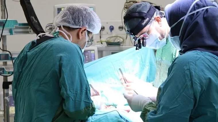 Ameliyat masasında, cerrahlar yeşil ameliyat giysileriyle çalışıyor.