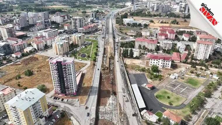 Sivas'ta inşaat halindeki bir yol, çevresinde apartmanlar ve yeşil alanlar ile birlikte görünmekte.
