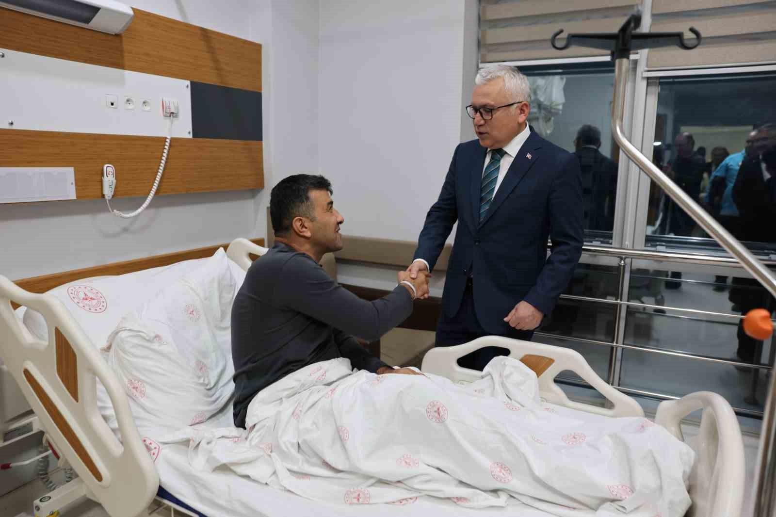 Hastane odasında yatakta oturan bir kişi, takım elbiseli bir kişiyle el sıkışıyor.