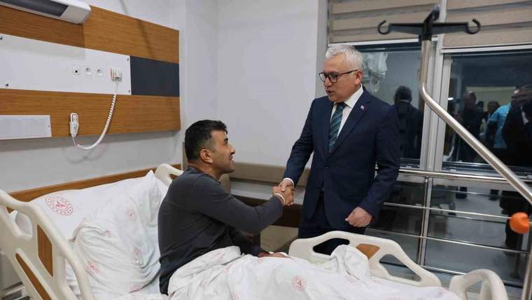 Hastane odasında yatakta oturan bir kişi, takım elbiseli bir kişiyle el sıkışıyor.