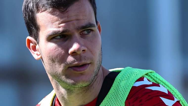 Kırmızı forma ve yeşil antrenman yeleği giyen bir futbolcunun saha kenarındaki yakın plan görüntüsü