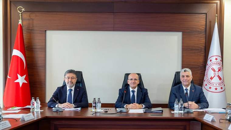 Toplantı masasında oturan üç erkek, Türk bayrağı ve üzerinde kurum amblemi bulunan bayrakla birlikte görülüyor.