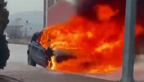 Sokak kenarında duran bir otomobilin ön ve üst bölümü yoğun alevler içinde yanıyor.