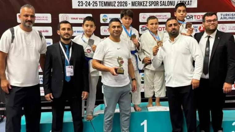Bir grup çocuk ve yetişkin, ödül töreninde madalyalarını tutarak gülümsüyor.