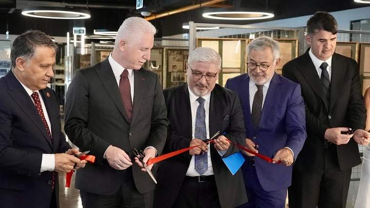Kapalı bir alanda beş erkek, kırmızı kurdeleyi makaslarla keserken yan yana duruyor.