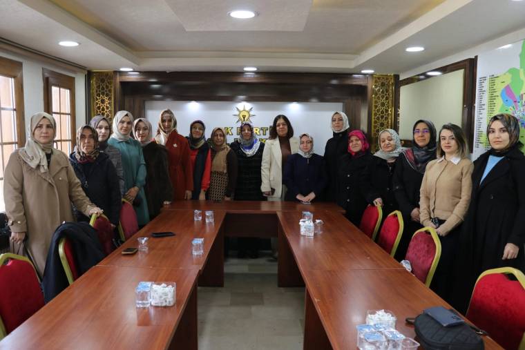 Toplantı salonunda uzun masanın çevresinde duran kadınlar, masalarda su şişeleri ve sandalyeler görülüyor.