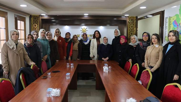 Toplantı salonunda uzun masanın çevresinde duran kadınlar, masalarda su şişeleri ve sandalyeler görülüyor.