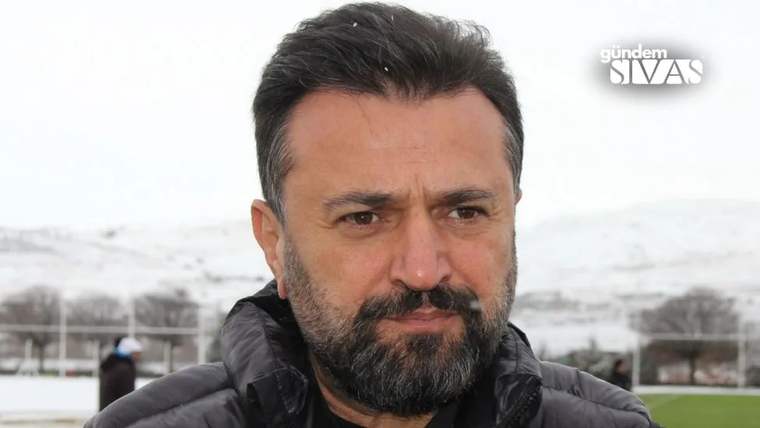 Sakallı bir adam, açık havada siyah montuyla kameraya bakıyor; arka planda karlı tepeler ve saha görülüyor.