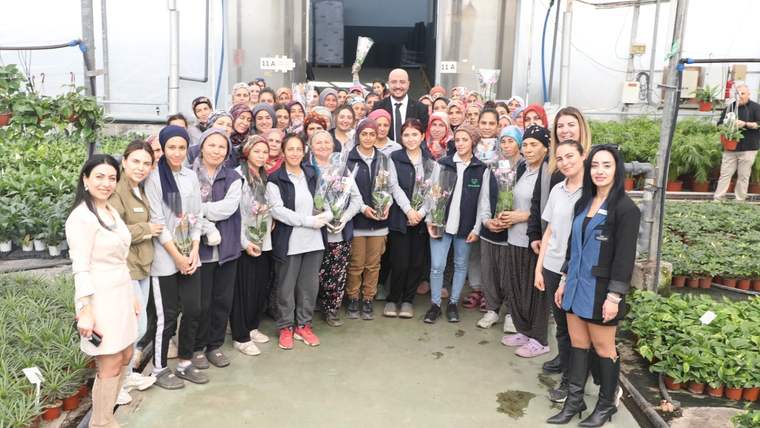 Serada, ellerinde çiçekler bulunan kalabalık bir grup, kameraya doğru yan yana duruyor.
