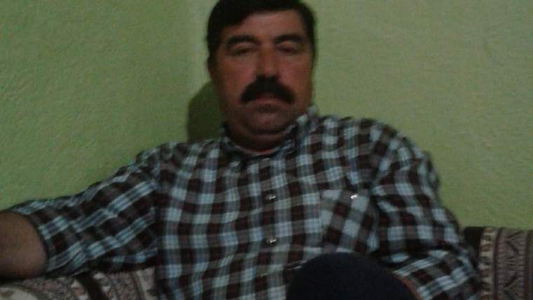Kareli gömlek giymiş bir adam, bir kanepeye oturmuş, duvara yaslanmış şekilde duruyor.