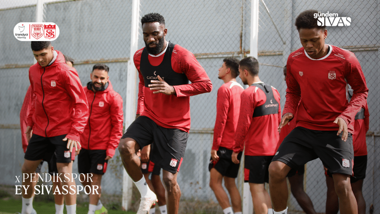 Antrenman yapan Sivasspor futbolcuları, kırmızı formalar giymiş. Arka planda bir saha ve tel örgü görünmekte.