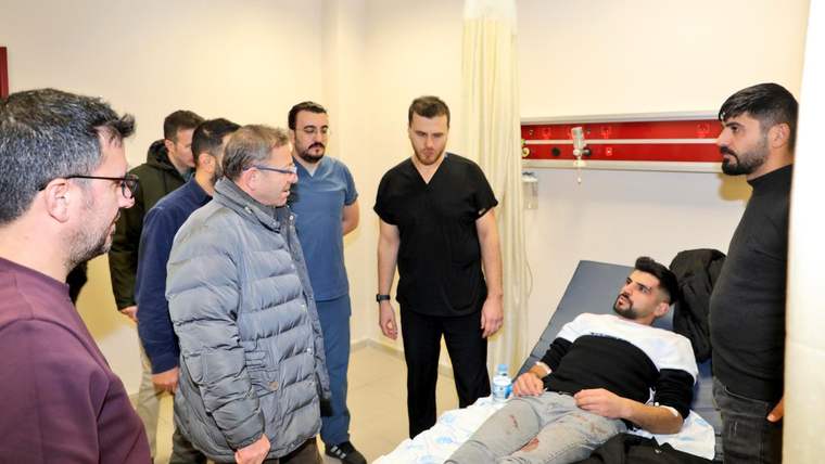 Hastane odasında yatağındaki yaralı kişinin çevresinde duran sağlık çalışanları ve ziyaretçiler görülüyor.