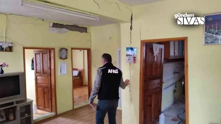 AFAD yazılı yelek giyen kişi, çatlak duvarlı bir evin koridorunda inceleme yapıyor.