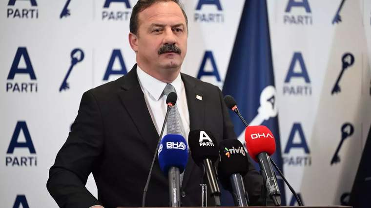 Takım elbiseli, bıyıklı bir kişi, üzerinde A Parti ve çeşitli medya logoları bulunan kürsüde konuşuyor.
