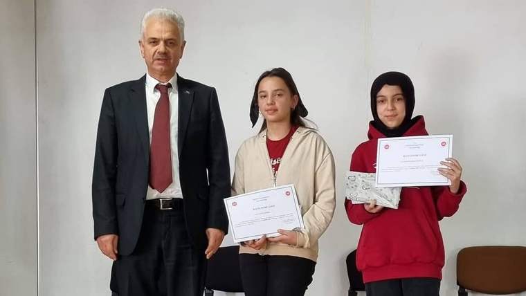 Takım elbiseli bir erkek, iki kız çocuğuyla birlikte ellerindeki başarı belgelerini gösteriyor.