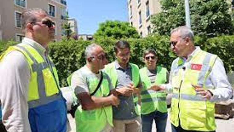 Yeşil yelek giymiş beş kişi, bir arada durarak konuşuyor.