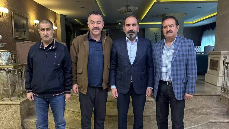 Dört kişi, bir otelin lobisinde yan yana duruyor. Arkada lamba ve dekoratif unsurlar var.