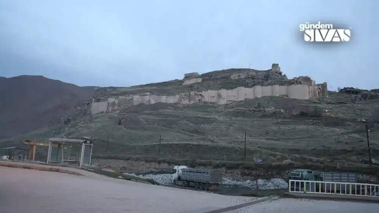 Divriği Kalesi, sarp bir tepe üzerinde yer alıyor ve çevresinde yeşil alanlar bulunuyor.