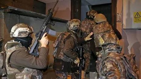 Askeri kıyafet giymiş birkaç kişi, kapıdan içeri girmeye çalışıyor.