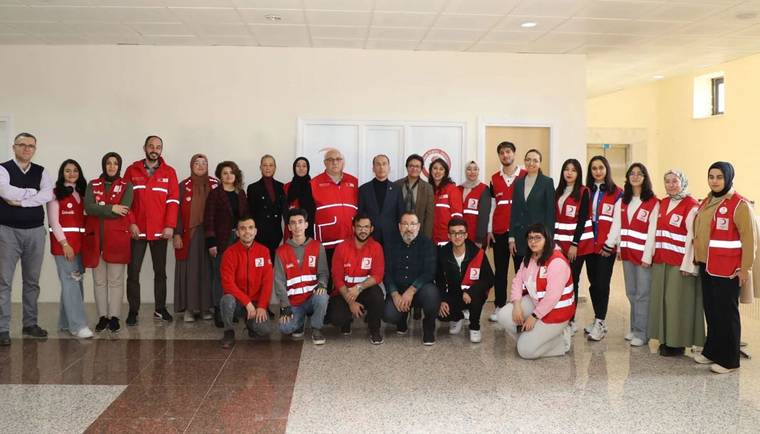 İç mekânda, kırmızı yelek ve kıyafetler giyen kalabalık bir grup birlikte poz veriyor.