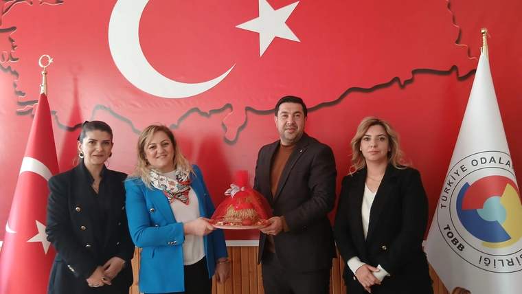 Türk bayrağı ve harita desenli duvar önünde dört kişi, ortadaki kişinin tuttuğu süslü tepsiyle poz veriyor.