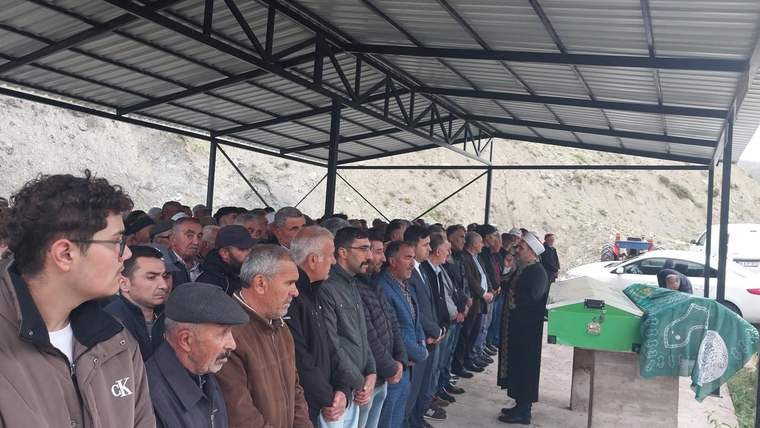 Bir grup insan, yeşil bir tabutun etrafında toplanmış, cenaze törenine katılıyor.