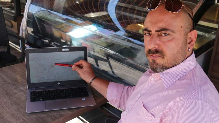 Pembe gömlekli bir kişi, dizüstü bilgisayar ekranındaki haritayı kırmızı kalemle gösteriyor.