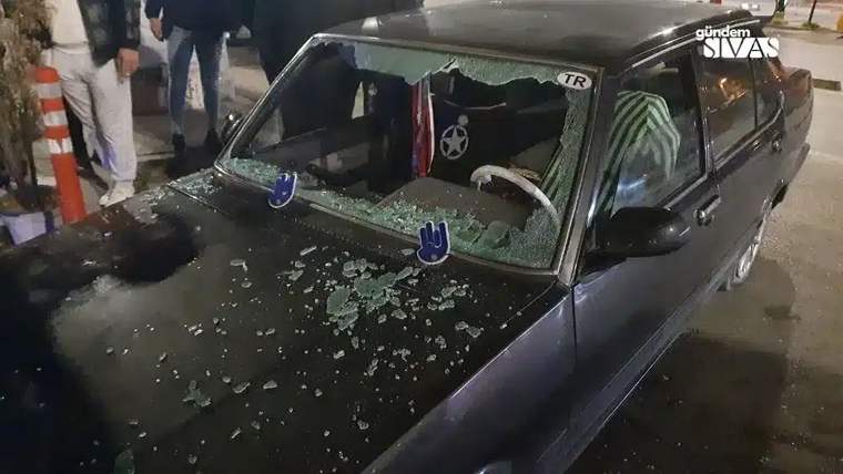 Kırık camları olan bir aracın üstünde taşlar ve cam parçaları bulunuyor.