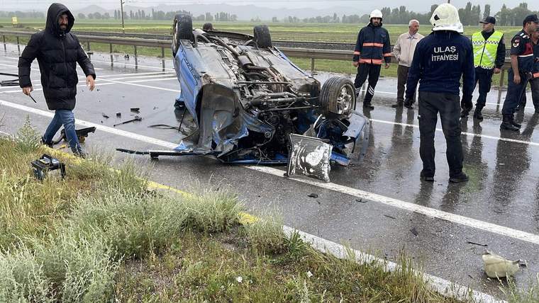 Yağışlı yolda ters dönmüş bir otomobilin çevresinde itfaiye görevlileri ve insanlar duruyor.