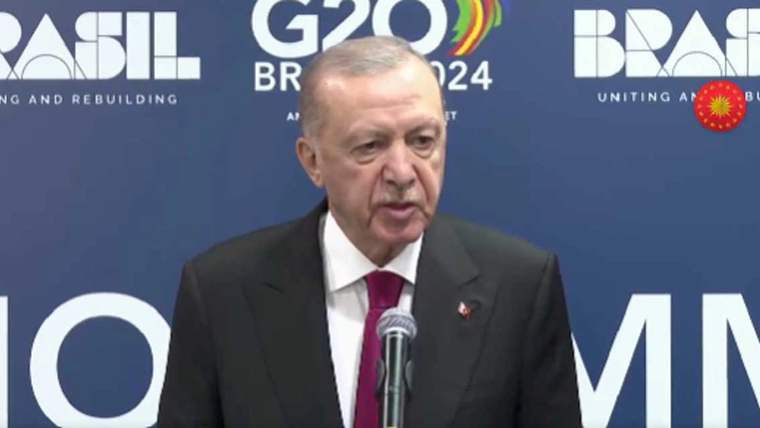 Mikrofonun önünde konuşan bir kişi, arkasında G20 logosu bulunan bir duvar var.