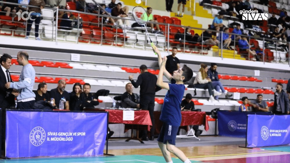 Badminton oynayan bir çocuk, spor salonunda raketle topa vuruyor.