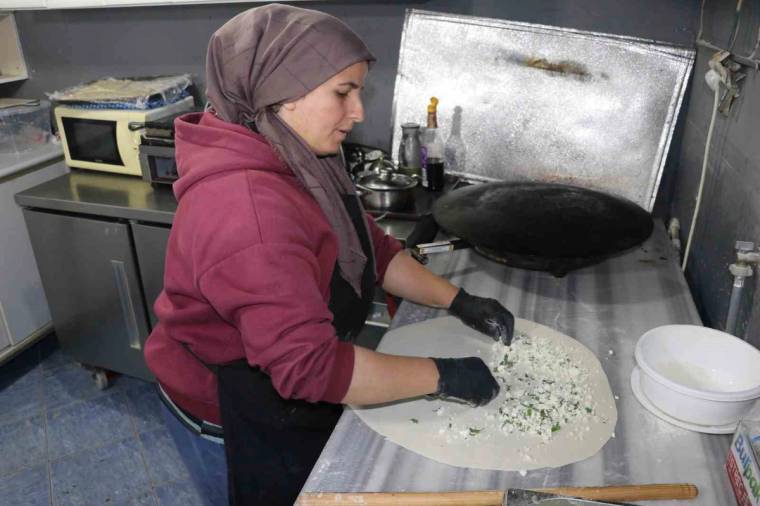 Başörtülü bir kadın, mutfak tezgâhında açılmış hamurun üzerine iç harç koyarak gözleme hazırlıyor.