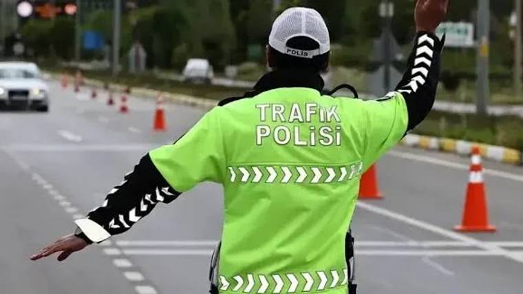 Trafik polisi, Sivas yolunda trafiği yönlendirmek için elini kaldırmış, arka planda koni ve yol işaretleri görünmekte.