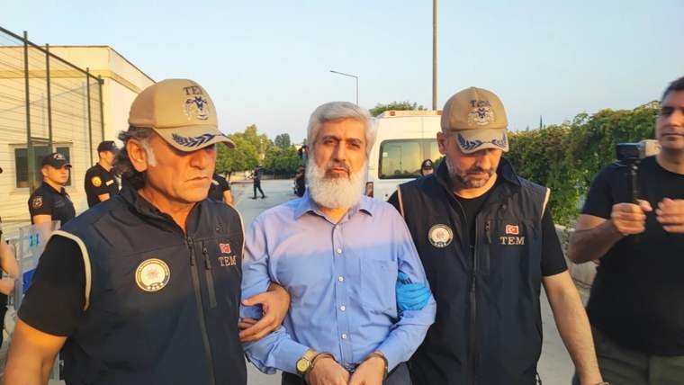 Üzerlerinde TEM yazılı yelekler bulunan iki görevli, sakallı bir erkeği kollarından tutarak yürütüyor.