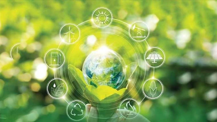Ellerin tuttuğu dünya küresi, yenilenebilir enerji simgeleri ve yeşil bitkilerle çevrili