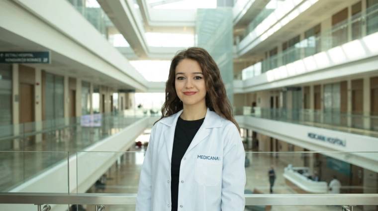 Hastane içindeki galeri boşluğunda, üzerinde “Medicana” yazan beyaz önlüklü bir kadın duruyor.
