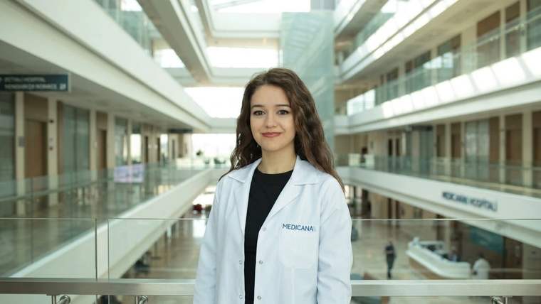 Hastane içindeki galeri boşluğunda, üzerinde “Medicana” yazan beyaz önlüklü bir kadın duruyor.
