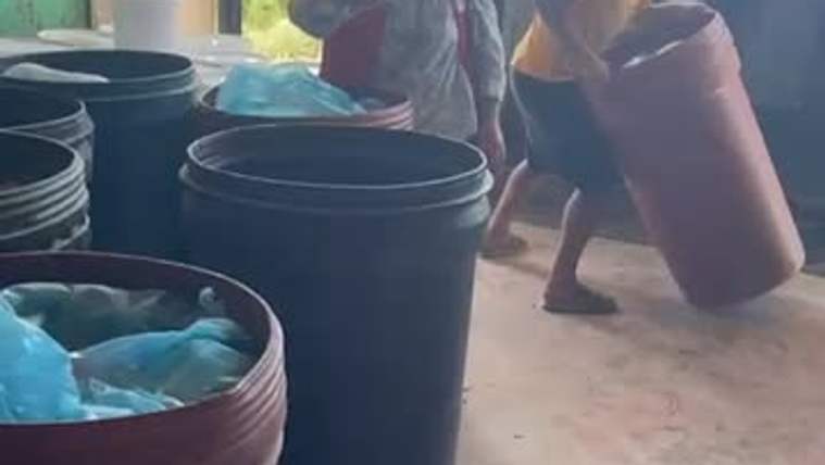 İç mekânda çok sayıda büyük plastik kova ve mavi poşet bulunurken bir kişi büyük bir kap taşıyor.